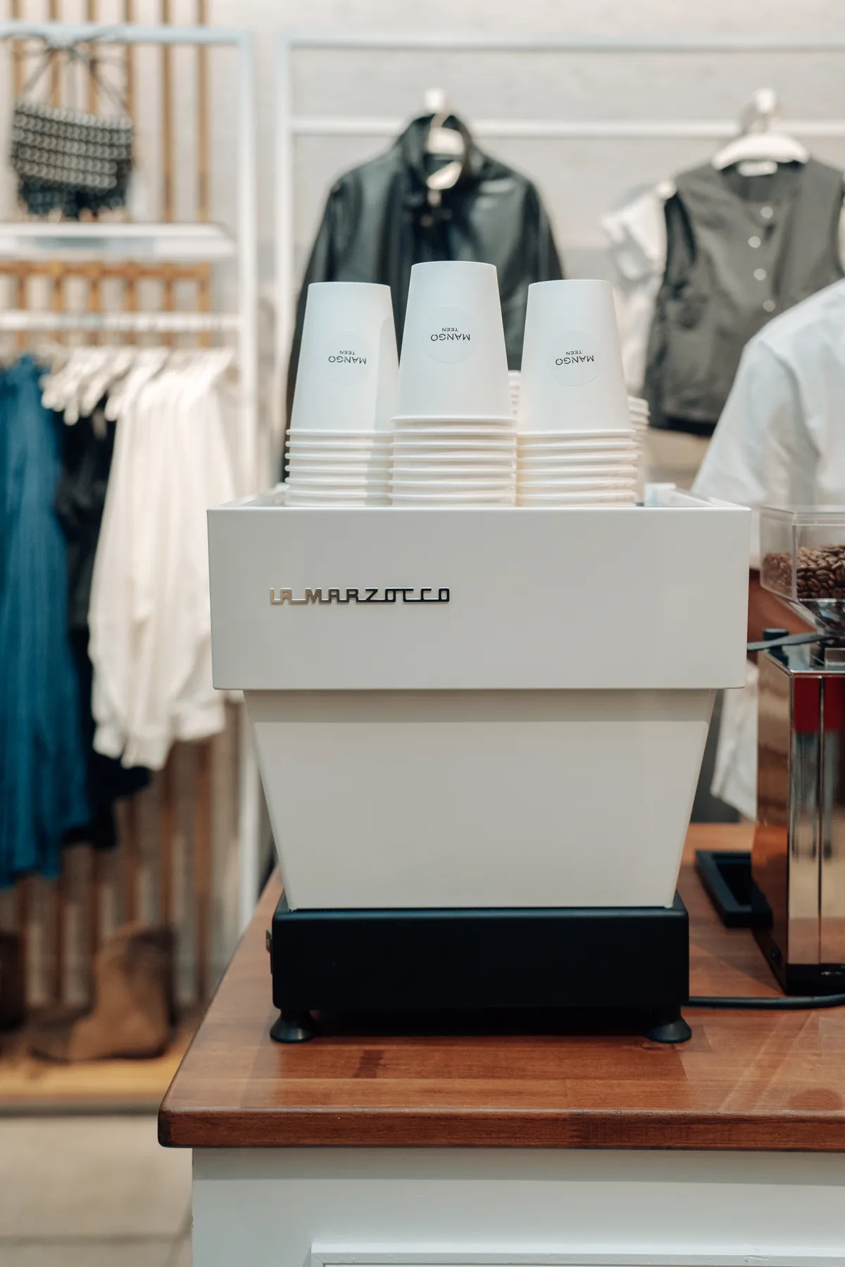 Machine espresso La Marzocco blanche surmontée de gobelets, sur un comptoir en bois